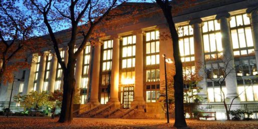 Harvard Law School Library at night shows an imposing building with columns and all the lights on against a darkening sky.