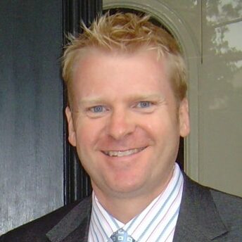 Man with short blonde hair wearing striped colored shirt.