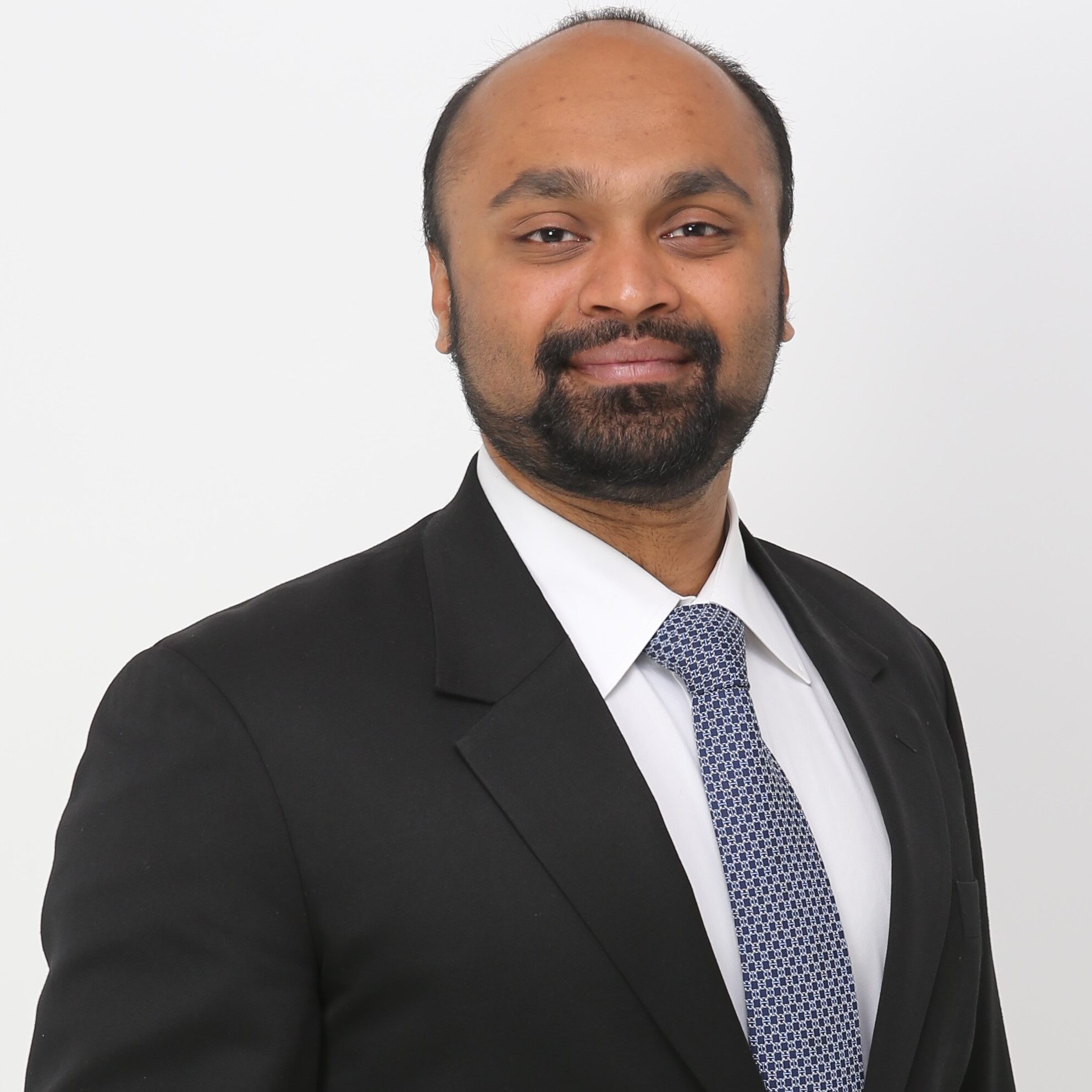 A young South Asian man wears a crisp suit and tie.