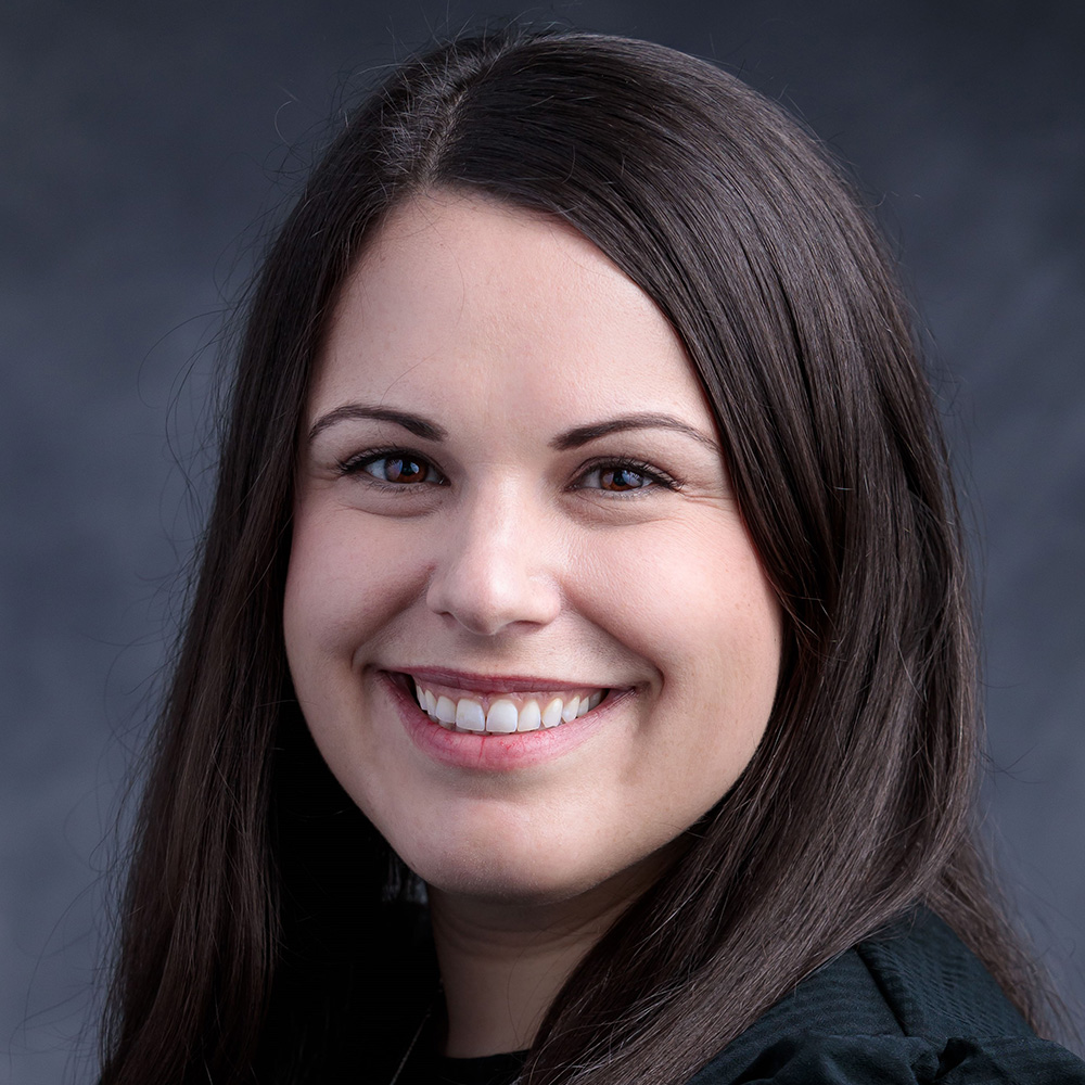 A white woman with brown hair smiles against a blue background.