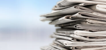 A stack of newspapers on the right against a blue blurry background.