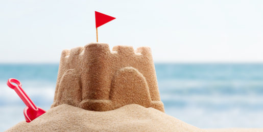 A sand castle with a red flag and a red shovel.