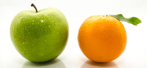 A green apple and an orange sit next to each other side by side.