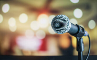 Microphone on a stand against a blurred lit up background.