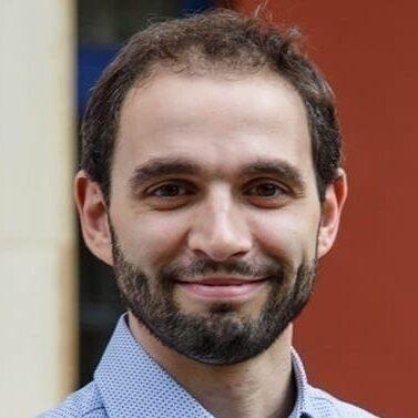 Man in blue shirt with beard smiling.