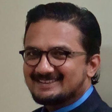 South Asian man with glasses and black hair.