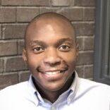 South African male sitting in front of brick wall.