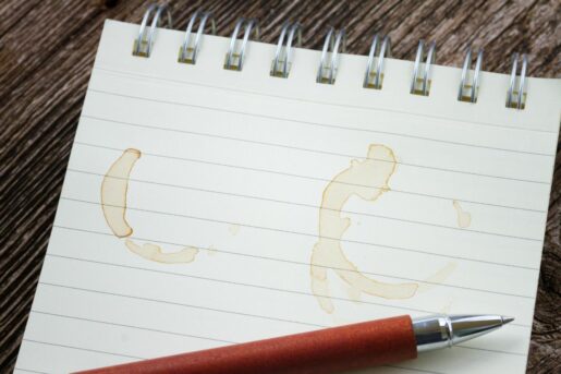 Image of a pen and opened notepad with some coffee stains.