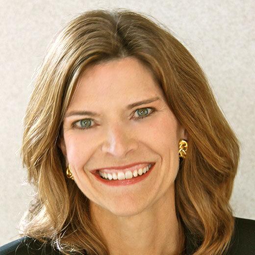 Broadly smiling woman with brown hair in a black suit.