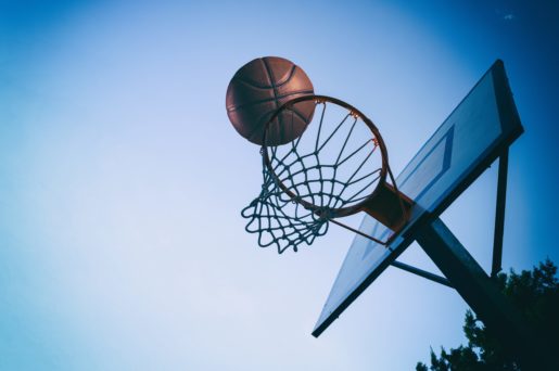 A ball enters a basketball hoop beneath a blue sky.