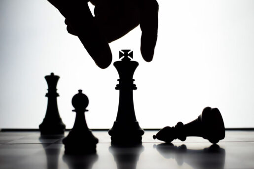 A hand moves a chess piece across the board while a pawn is on its side.