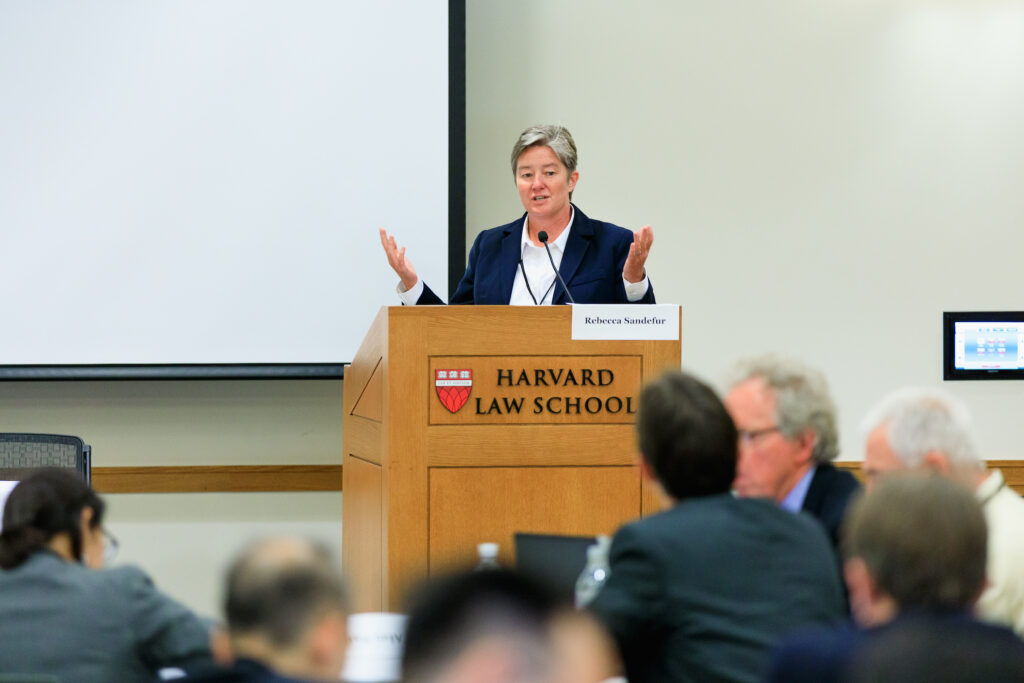 A woman gestures with her hands at a podium that says "Harvard Law School."