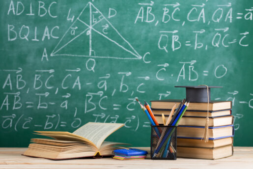 An image portraying a schoolroom, with a chalk board with equations, a stack of books, and a can of pencils.