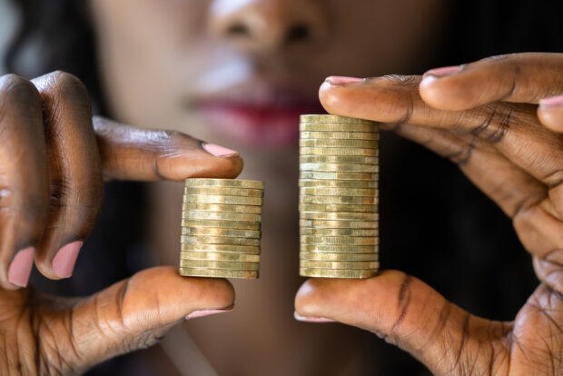 A Black woman holds two different stacks of coins comparing them—one is higher.