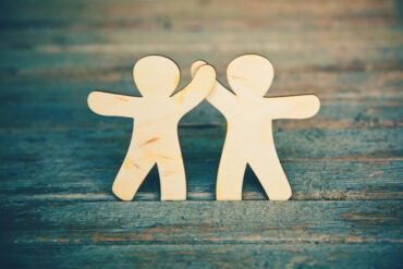 Two wooden figures high five.