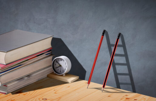 Books sit next to two pencils leaning against a wall, which forms a shadow showing a ladder.