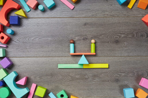 Two wooden toys balance on a seesaw amidst other wooden toys.