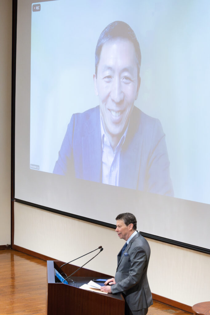 Goodwin Liu appears on screen while David B Wilkins stands at a podium.
