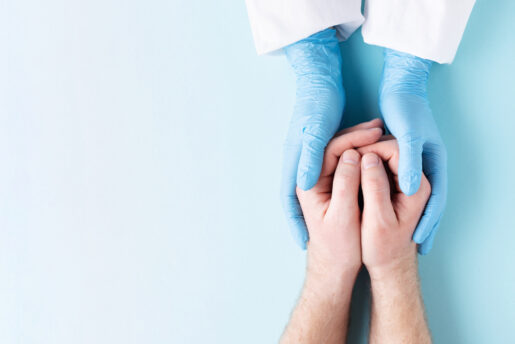 Gloved doctor hands hold ungloved hand, signaling collaboration between clinicians and others.