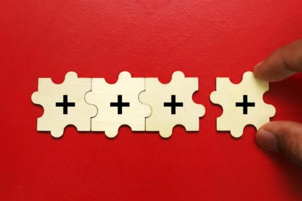 a hand places a final plus sign in an array of puzzle pieces.